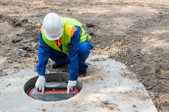 worker in a white helmet, closes the lid of the collector for communications