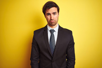 Young handsome businessman wearing suit and tie standing over isolated yellow background depressed and worry for distress, crying angry and afraid. Sad expression.