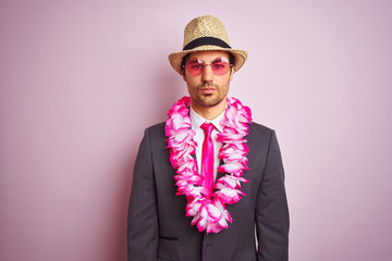 Young businessman wearing suit hat glasses hawaiian lei over isolated pink background with a...