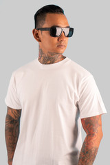 Black man wearing glasses wearing a white short sleeved t-shirt with tattoos on both arms and neck.