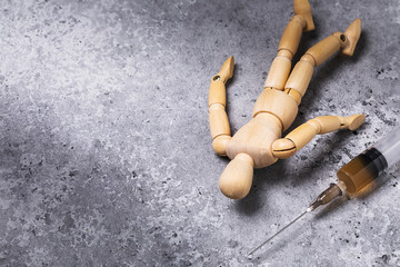 A syringe with drugs and next to it lies the figure of a man made of wood. Addict on the floor....