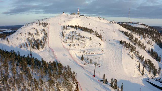 Aerial, tracking, drone shot, overlooking people skiing on the slopes, of the Rukatunturi fell, golden hour, on a sunny, winter evening, in Ruka, Lapland, Finland