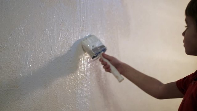 boy paints a wall with white paint with a brush. Video picture.