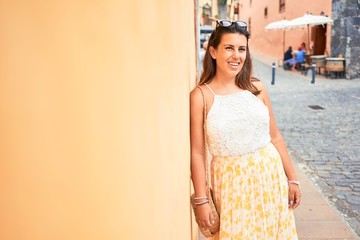 Fototapeta premium Beautiful girl leaning on orange wall, young friendly woman smiling happy on a sunny day of summer