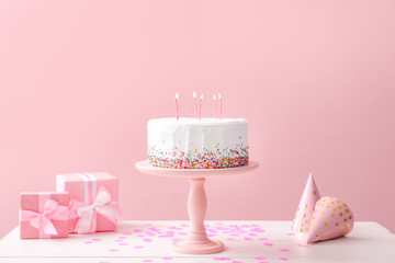 Tasty Birthday cake with gifts on table against color background