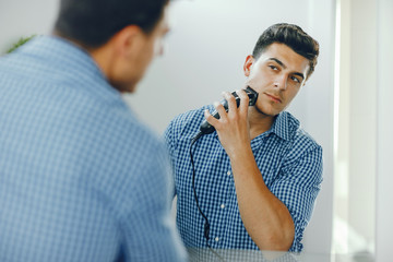 Man with an electric razor. The guy in the bathroom. Male in a bue shirt.