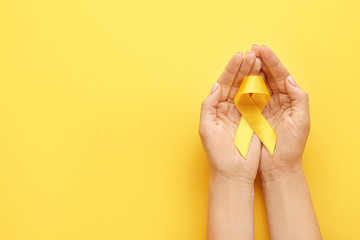 Female hands with yellow ribbon on color background. Cancer awareness concept