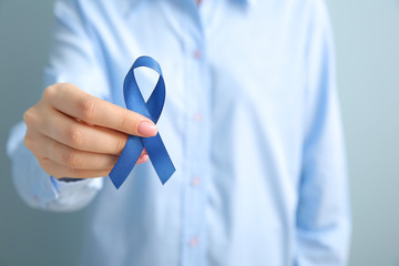 Young woman with blue ribbon on grey background, closeup. Cancer awareness concept