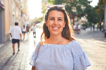 Young beautiful woman smiling happy walking on city streets on a sunny day of summer