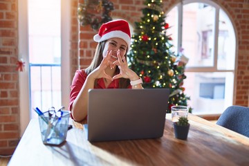 Beautiful woman sitting at the table working with laptop wearing santa claus hat at christmas smiling in love showing heart symbol and shape with hands. Romantic concept.