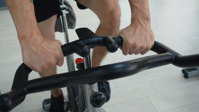 Male hands holding handle static bike in fitness club. Sportsman training gym bicycle on indoor bike in gym. Fitness man setting bike on cycling class