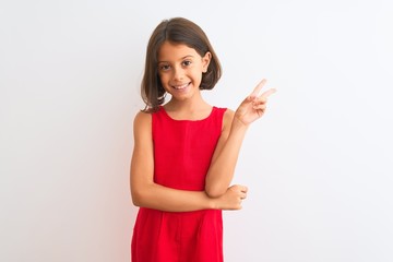 Young beautiful child girl wearing red casual dress standing over isolated white background smiling with happy face winking at the camera doing victory sign. Number two.