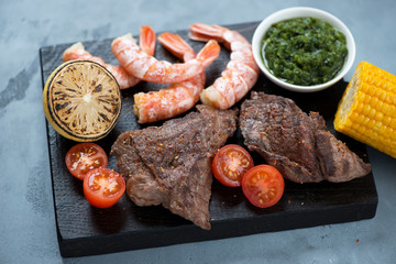 Surf and turf with marbled beefsteaks, shrimps, cherry tomatoes, corn, lemon and chimichurri, studio shot