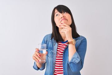 Young beautiful Chinese woman holding glass of water over isolated white background serious face thinking about question, very confused idea