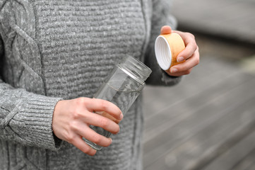 close-up of female hands in a woolen sweater opening a refillable glass water bottle - 303759625