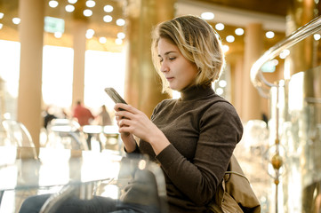 young european girl is chatting online by phone in a cafe mall