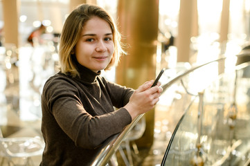 young european girl smiles and is chatting online by phone in a cafe mall