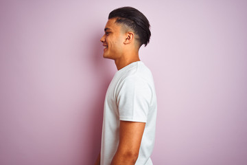 Young brazilian man wearing t-shirt standing over isolated pink background looking to side, relax...
