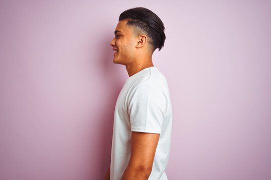 Young brazilian man wearing t-shirt standing over isolated pink background looking to side, relax profile pose with natural face with confident smile.