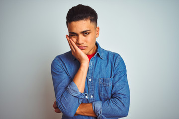 Young brazilian man wearing denim shirt standing over isolated white background thinking looking tired and bored with depression problems with crossed arms.