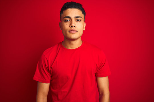 Young brazilian man wearing t-shirt standing over isolated red background Relaxed with serious expression on face. Simple and natural looking at the camera.