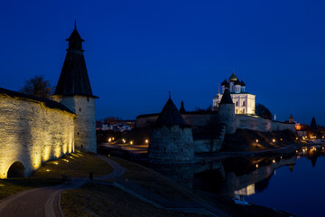 Night panorama of the city. Lanterns illuminate the walls and towers of the medieval fortress and are reflected in the water of the river. Pskov, Russia.