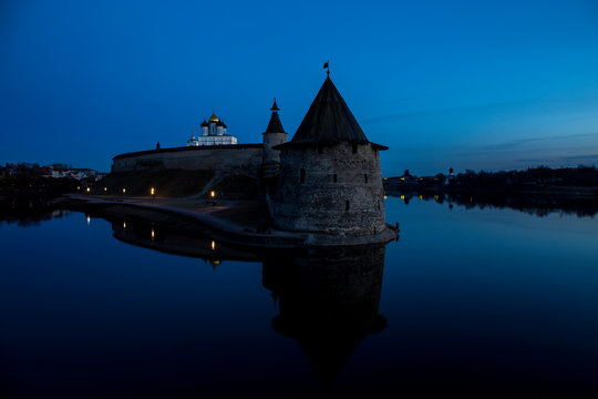 Night panorama of the city. Lanterns illuminate the walls and towers of the medieval fortress and are reflected in the water of the river. Pskov, Russia.