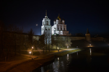 Night panorama of the city. Lanterns illuminate the walls and towers of the medieval fortress with a bell tower and a Cathedral which are reflected in the water of the river. Pskov, Russia.