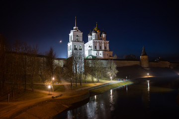 Fototapeta na wymiar Night panorama of the city. Lanterns illuminate the walls and towers of the medieval fortress with a bell tower and a Cathedral which are reflected in the water of the river. Pskov, Russia.