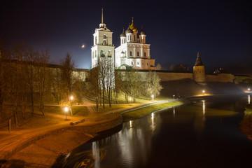 Night panorama of the city. Lanterns illuminate the walls and towers of the medieval fortress with a bell tower and a Cathedral which are reflected in the water of the river. Pskov, Russia.