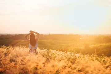 Fototapeta na wymiar Trendy girl in stylish summer dress feeling free in the field with flowers in sunshine.