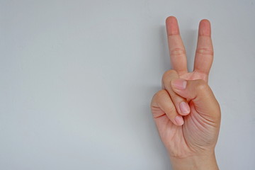 Close-up of female hand showing two fingers isolated on grey background. Side view close up details.