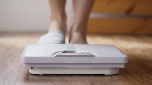 Close up of young Asian woman checking body weight on weighing scale in the living room at home.