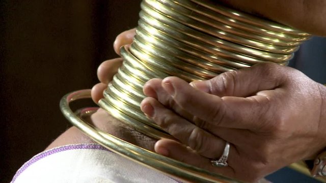 A daylight extreme closeup shot of layers of gold rings being coiled around the neck of a native woman of Kayan (Padaung).