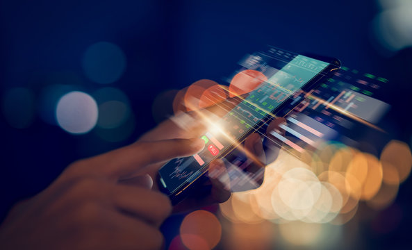 Stock exchange market concept, hand trader touching on smartphone with graphs analysis candle line on bokeh colors light in night atmospheric city.