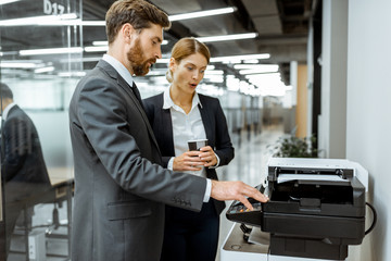 Business man and woman talking near the copier during a coffee break in the hallway of the big...