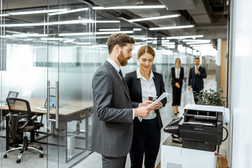 Business man and woman talking near the copier during a coffee break in the hallway of the big...