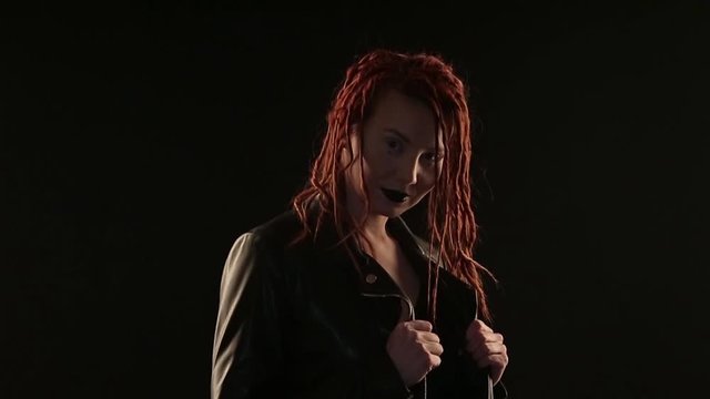 concept dances, parties, advertising leather jackets, styling hair, hairdressing dreadlocks, make-up: dark lipstick. rocker dancing on black background, woman styling red hair