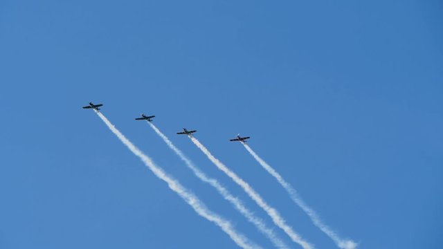 Propeller-driven aircrafts establish performance at an air show by releasing a smoke screen. Vehicles make extreme maneuvers and dead loops. Airsraft flying in sky.