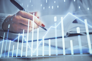 Multi exposure of woman's hands making notes with forex graph hologram. Concept stock market analysis.