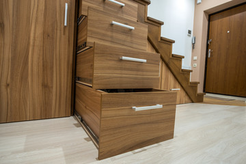 Modern architecture interior with luxury hallway with glossy wooden stairs in multi-storey house. Custom built pullout cabinets on glides in slots under stairs. Use of space for storage.