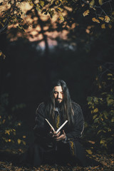 A man with long hair and beard in a black cloak in the image of a sorcerer warlock on Halloween....
