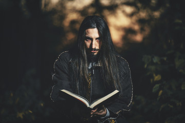 A man with long hair and beard in a black cloak in the image of a sorcerer warlock on Halloween....
