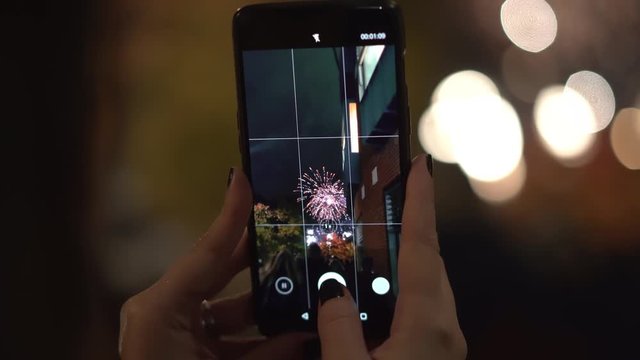 A woman captures fireworks on video, in super close up.