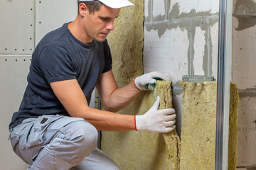 Worker insulating a room wall with mineral rock wool thermal insulation.