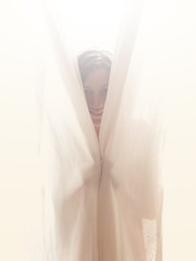 Woman hiding behind the window curtain indoors.