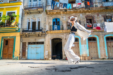 Stylish woman in a white suit and white hat dancing on an city street of Cuba