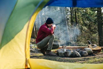 Image of a view from tent entrance of young man traveler drinks coffee with overlook amazing of forest, beautiful and inspiring camp location. Explore travel real wilderness lifestyle