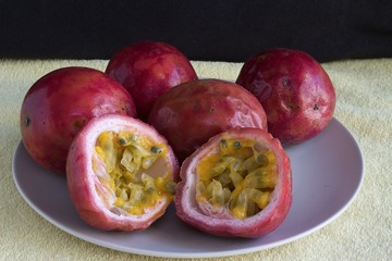 Fototapeta na wymiar Some passion fruit on a plate. One of the fruit is cut in half, showing its interior