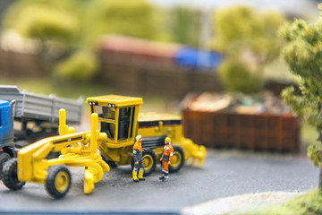 Layout of the city and small figures. Yellow tractor on the street next to the workers